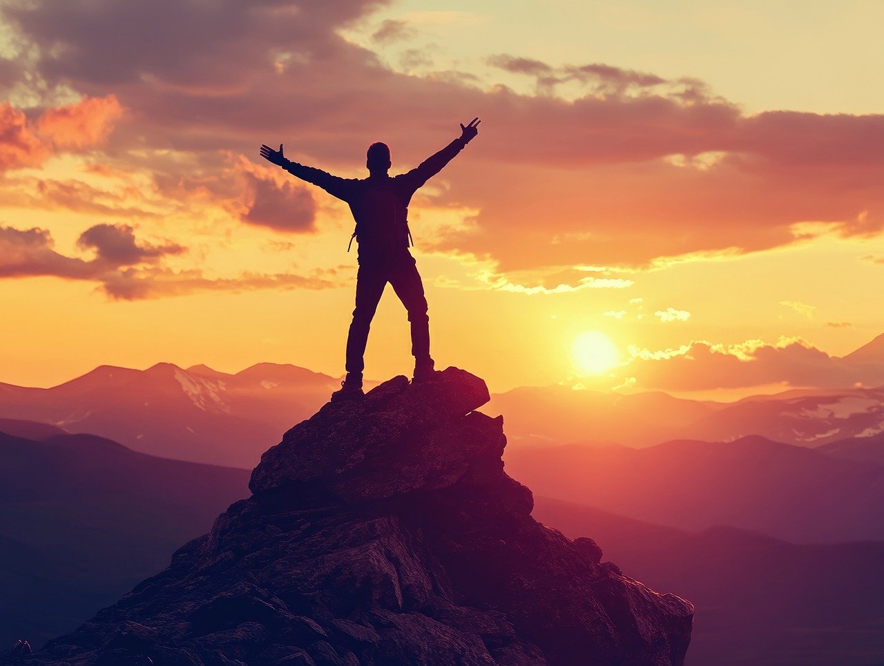 Person standing triumphantly on top of a mountain at sunset, symbolizing success, motivation, and personal achievement.